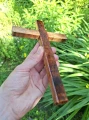 Krzyż drewniany na ścianę, handmade - drzewo egzotyczne - 22 cm - w naturalnym świetle na tle zieleni.